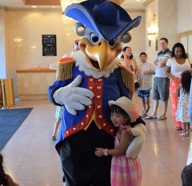 An eagle mascot poses for a photo with a young girl in a hat.