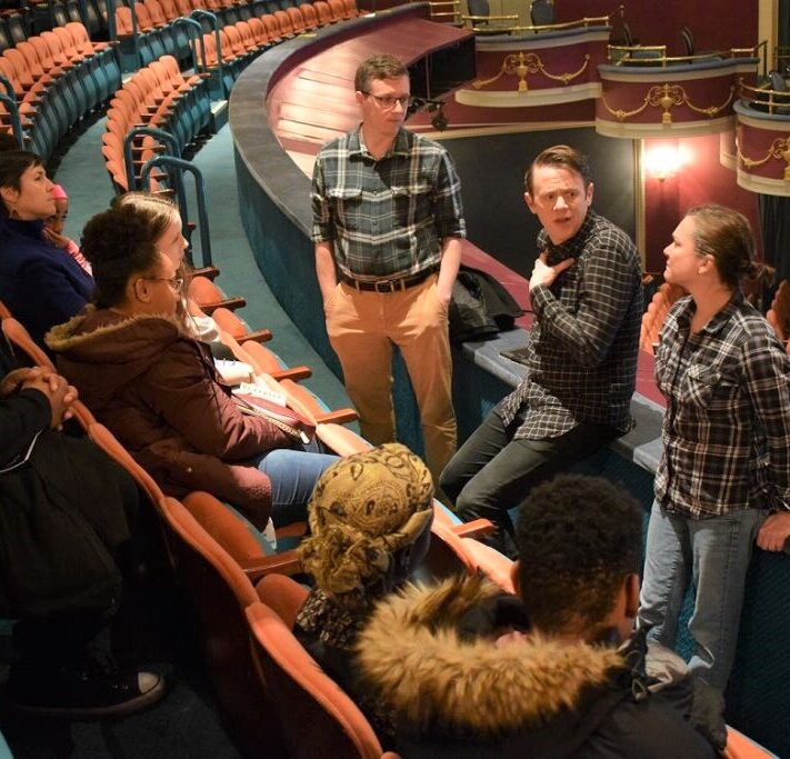 Students sit in auditorium seats listening as cast members share stories from a production.