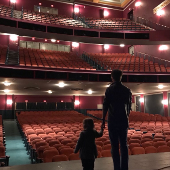 Father and daughter stand on the stage looking out to the empty theatre.