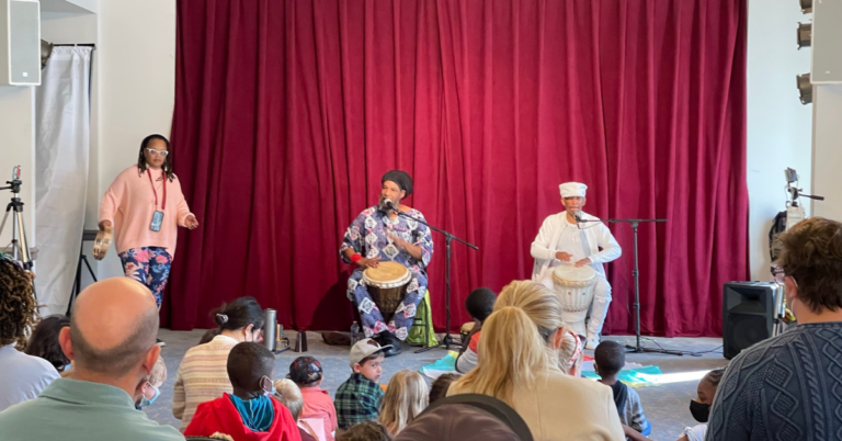 Three performers drum for a crowd of children