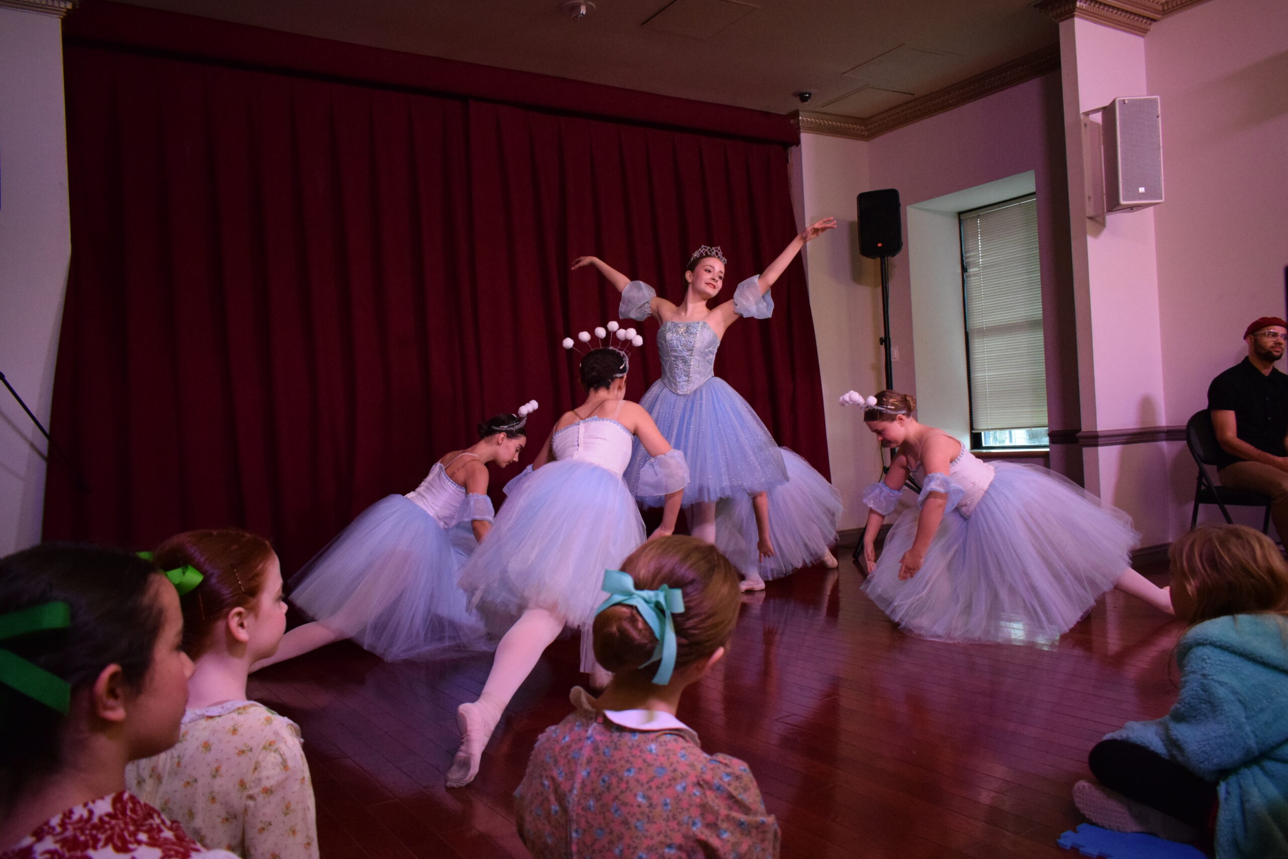 Ballerinas in shimmering gowns pose dramatically, with the central dancer standing tall with her arms outstretched.