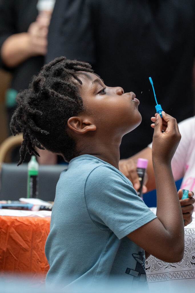 A young boy in a light blue shirt blows bubbles.