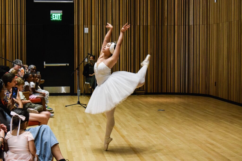 A ballerina in a white tutu and headband strikes a pose.