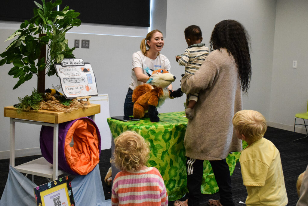 A young woman with a fox puppet greets parents and children.