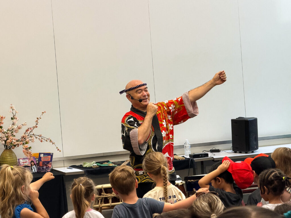 A man in a traditional red Japanese top teaches young children some dance moves.